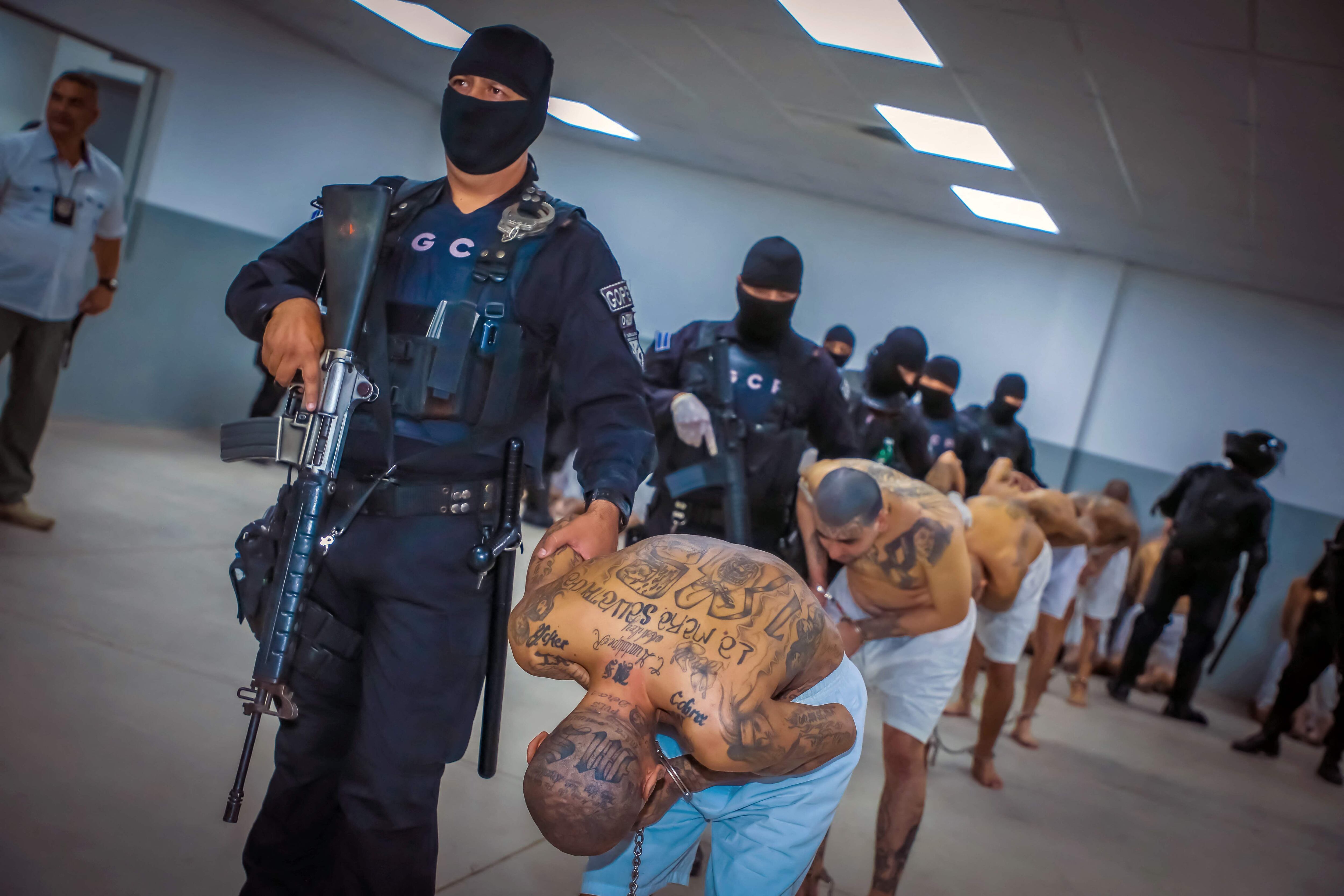 Foto informativa difundida por la Secretaria de Prensa de la Presidencia de El Salvador que muestra a policías escoltando a internos de las pandillas MS-13 y 18 a su llegada al nuevo penal "Centro de Confinamiento de Terroristas" (CECOT), en Tecoluca, a 74 km al sureste de San Salvador, el 24 de febrero de 2023.