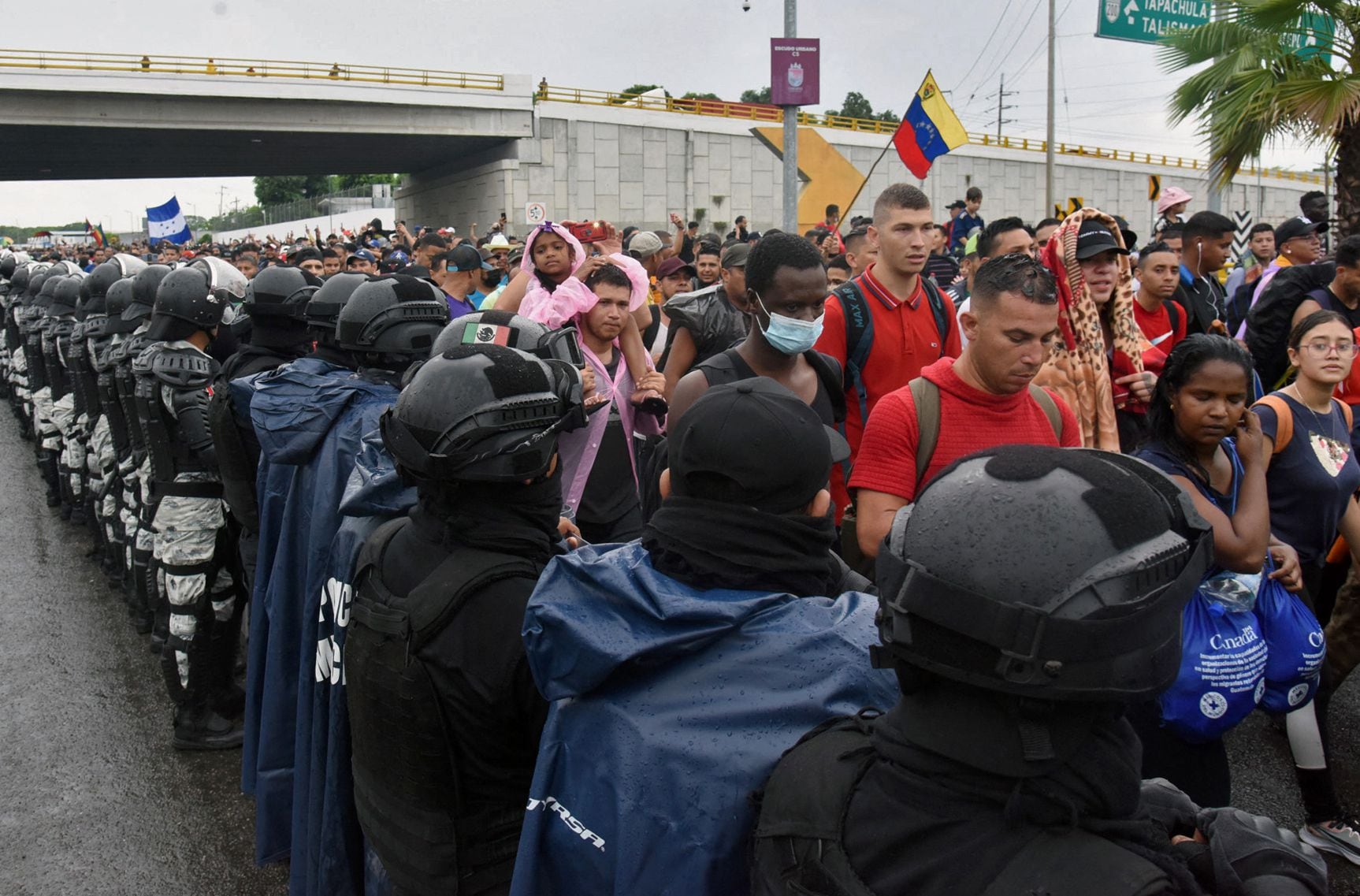 Miembros de la Guardia Nacional aparecen apostados mientras migrantes de América Central y del Sur con una bandera venezolana forman parte de una caravana hacia la frontera con Estados Unidos, en Tapachula, estado de Chiapas, México, el 6 de junio de 2022. (Foto de ISAAC GUZMAN / AFP )