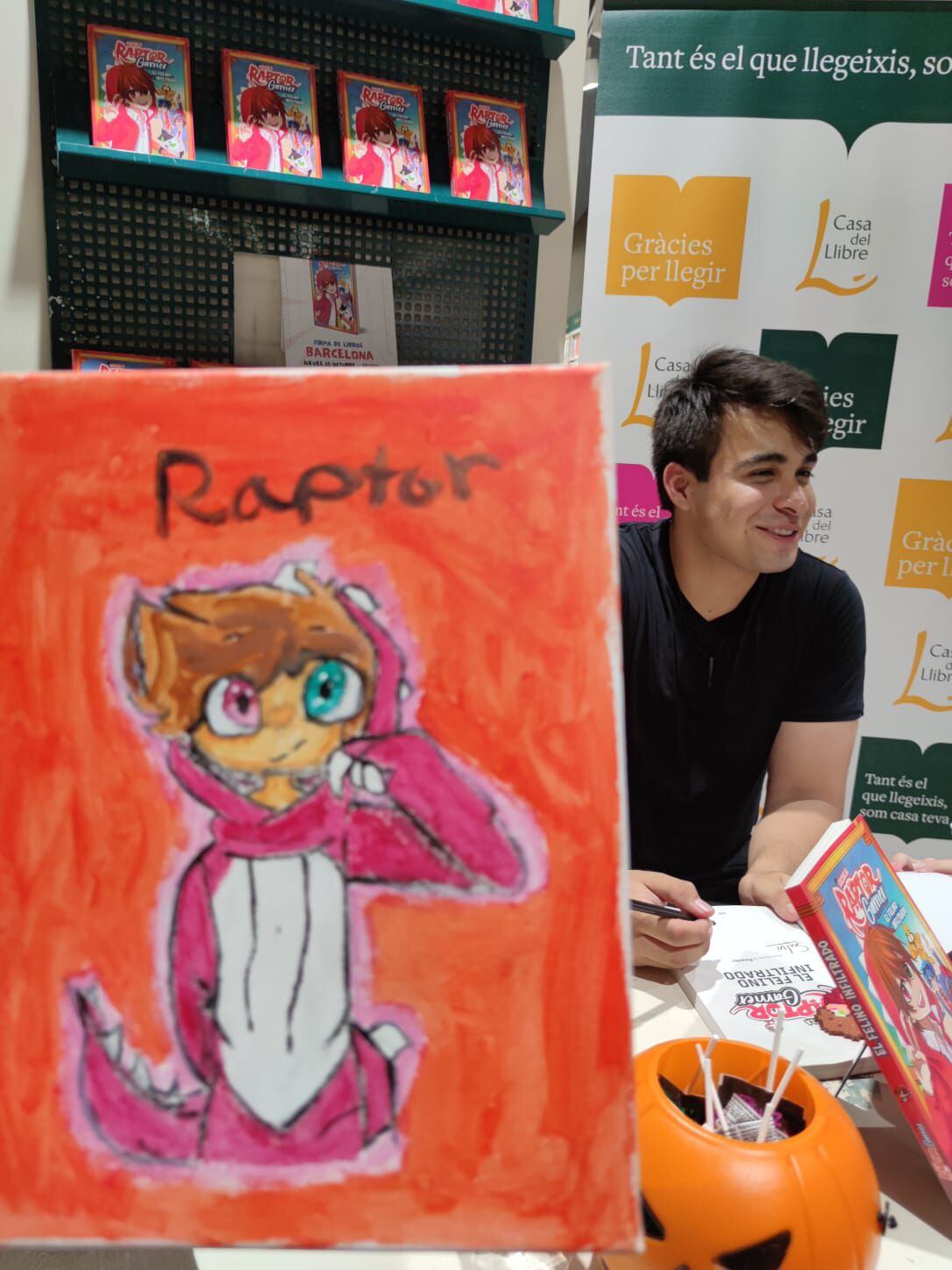 RaptorGamer (Ari Coronel) junto a una pieza de 'fanart' (arte aficionado) durante su firma de 'El felino infiltrado'. 