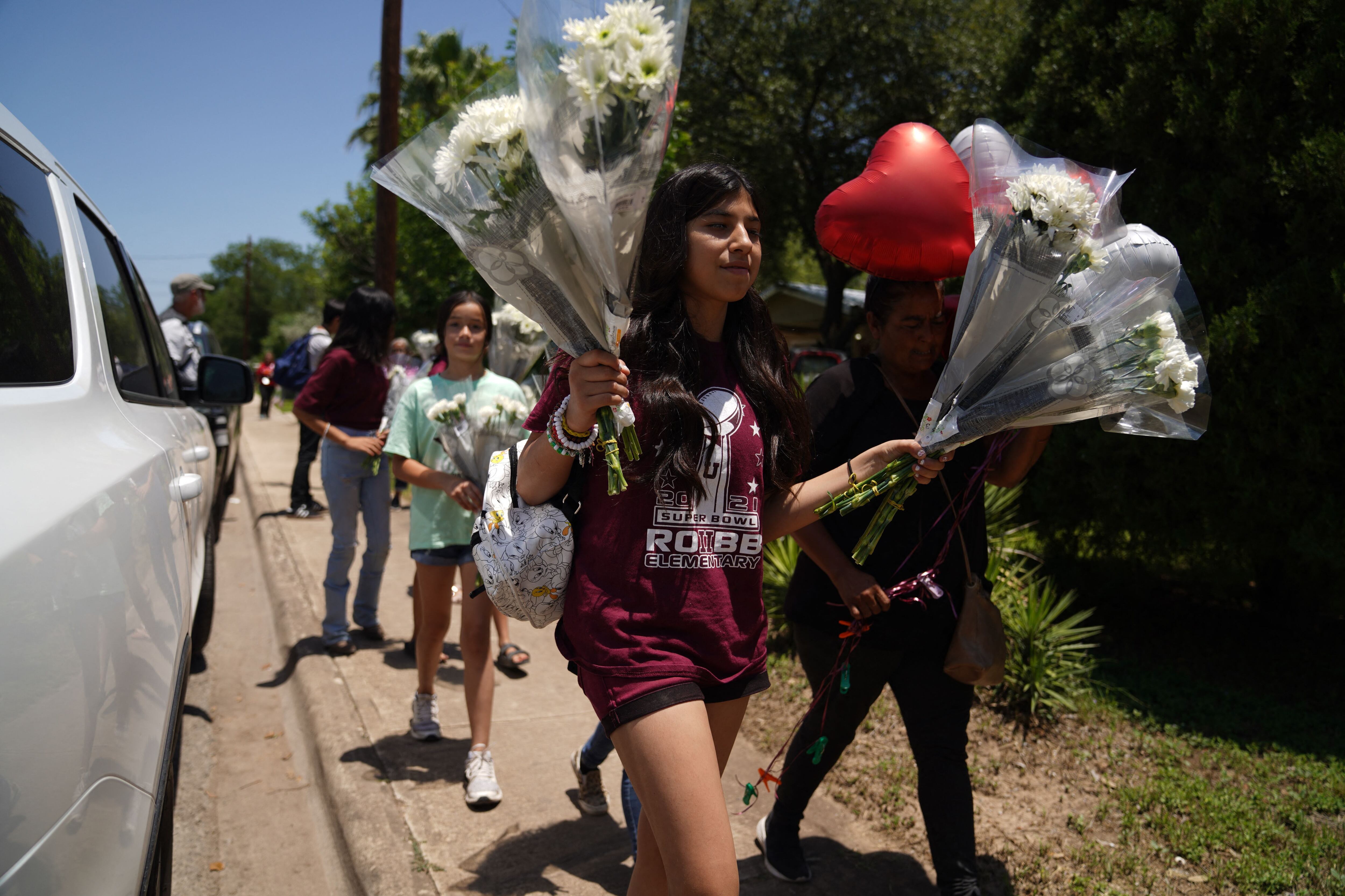 Gente llega para dejar flores en un monumento improvisado afuera de la Escuela Primaria Robb en Uvalde, que el 24 de mayo se convirtió en el lugar del peor tiroteo en una escuela en una década, cometido por un joven perturbado de 18 años armado con un rifle de asalto comprado legalmente. (Foto de Allison Dinner / AFP)