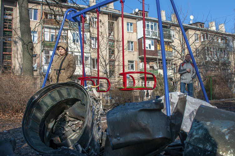 Un hombre y una mujer están de pie junto a fragmentos de equipo militar en la calle tras un ataque ruso en Kharkiv en Ucrania, el 24 de febrero de 2022. (AP Photo/Andrew Marienko)